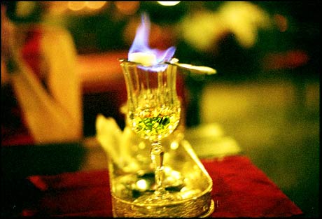 absinthe in glass sugar on fire on spoon red velvet brass tray
